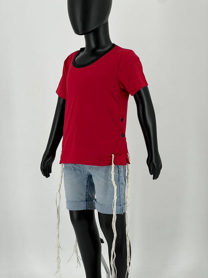 Mannequin wearing a red round-neck short-sleeve Tzitzit T-shirt with black side buttons, paired with light blue denim shorts. Four white Tzitzit fringes hang from the corners of the shirt in accordance with traditional Jewish practice. Displayed against a plain light background.