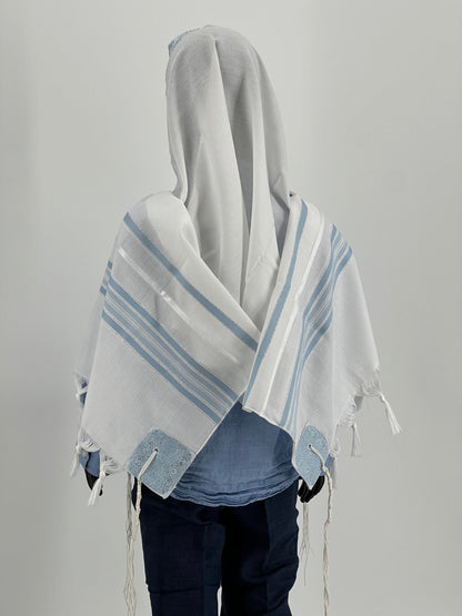 view of a child mannequin wearing a white tallit prayer shawl with light blue stripes and decorative corner reinforcements