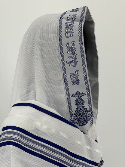Close-up side view of a white children's tallit (Jewish prayer shawl) with dark blue stripes and a decorative atara