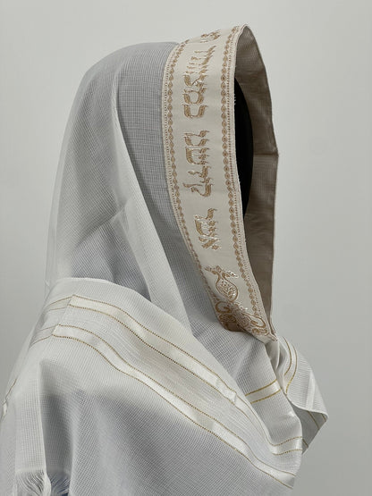 Child mannequin wearing a white tallit with an embroidered gold Hebrew blessing along the edge of the hood.