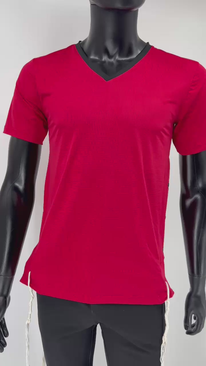 Video of a red athletic Tzitzit T-shirt with a black V-neck, worn by a black mannequin. The shirt features side snap closures and traditional white Tzitzit strings hanging from the hem, combining halachic requirements with a modern sporty design.