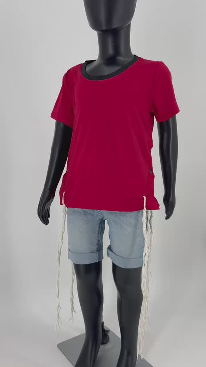 Video of Mannequin dressed in a red round-neck short-sleeve Tzitzit T-shirt with a breathable mesh texture, featuring white Tzitzit fringes hanging from the garment's corners. The shirt includes white side buttons and is paired with light blue denim shorts. Displayed against a plain light background.